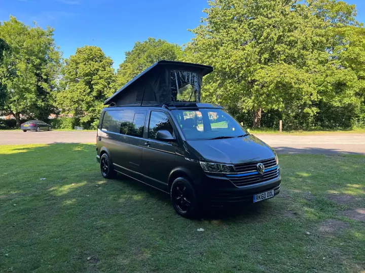 Czarny VW T6 z rozłożonym dachem podnoszonym na trawie w parku